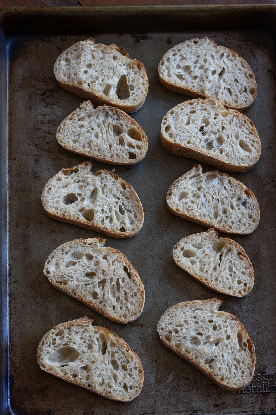 Baguette sliced and on a baking sheet ready to be toasted in the oven.