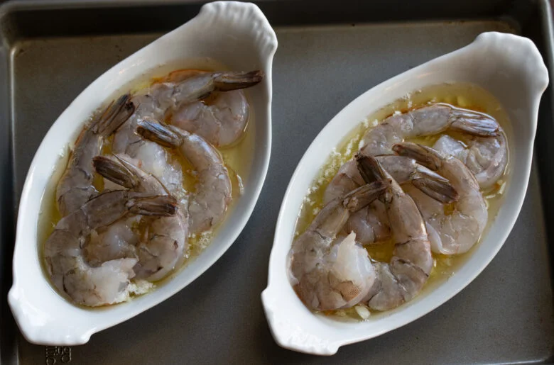 Raw shrimp placed in the hot gratin dishes ready to go back into the oven .