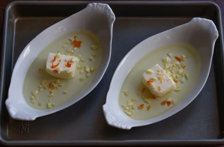 Butter, oil, garlic and chili pepper placed in gratin dishes on a rimmed baking dish.