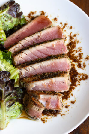 Grilled tuna steak sliced and fanned out on a white plate with salad alongside.