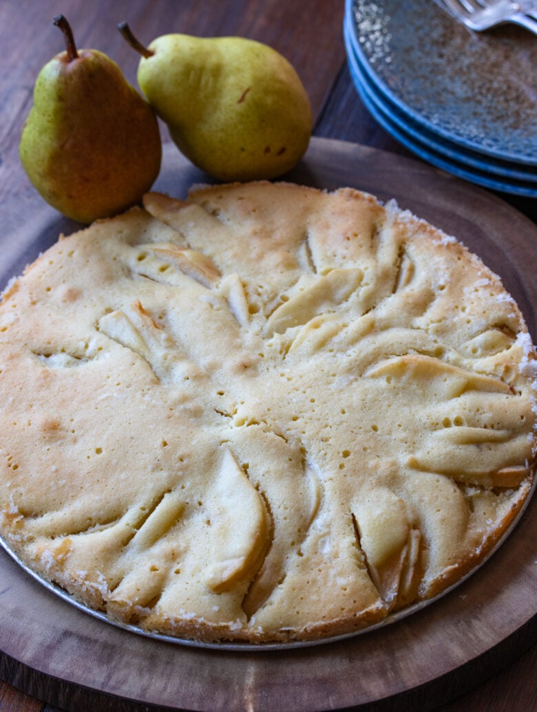 Pear cake on a wooden plate ready to be enjoyed, and blue small plates alongside.