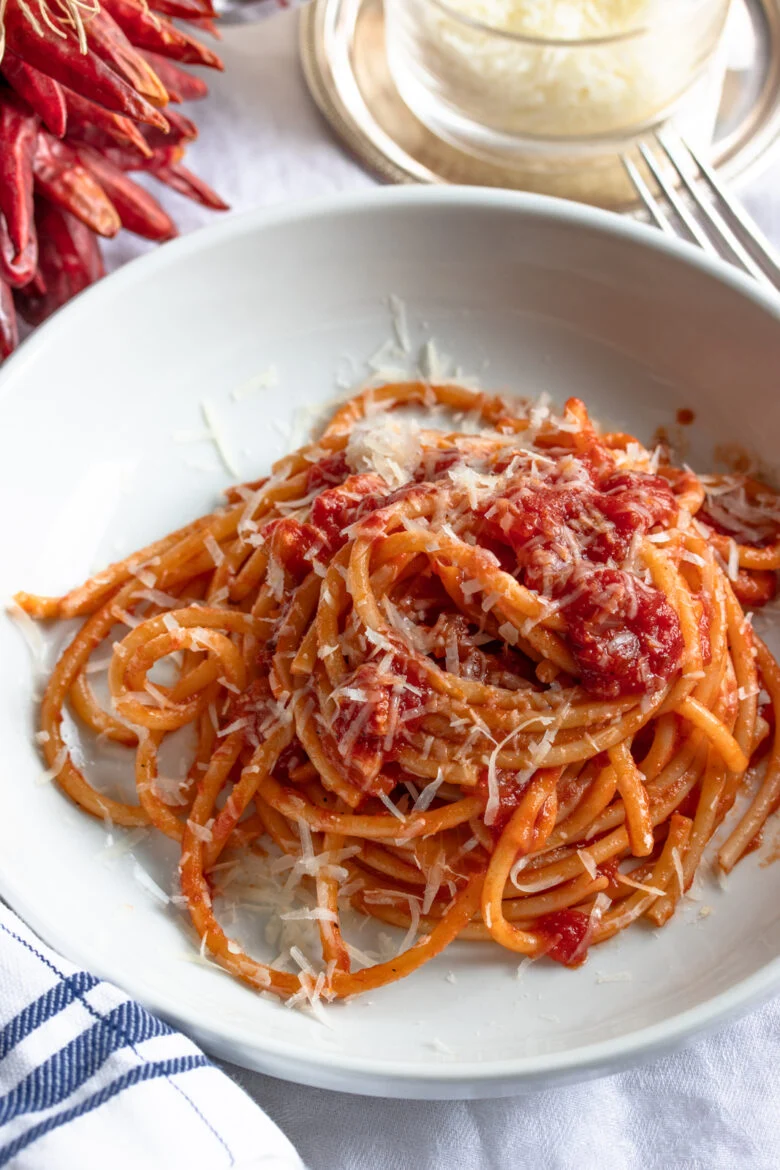 Bucatini all' Amatriciana served in a white plate with freshly grated cheese near by.