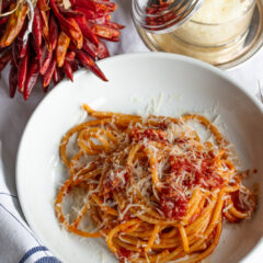 Bucatini all'amatriciana served on a white place with grated pecorino cheese next to it.