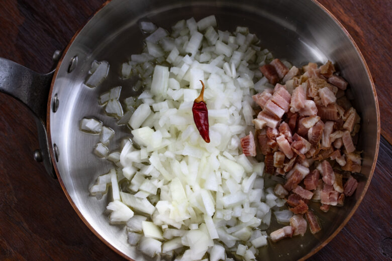 Chopped onions, pancetta and chili pepper in a large skillet raedy to be cooked.