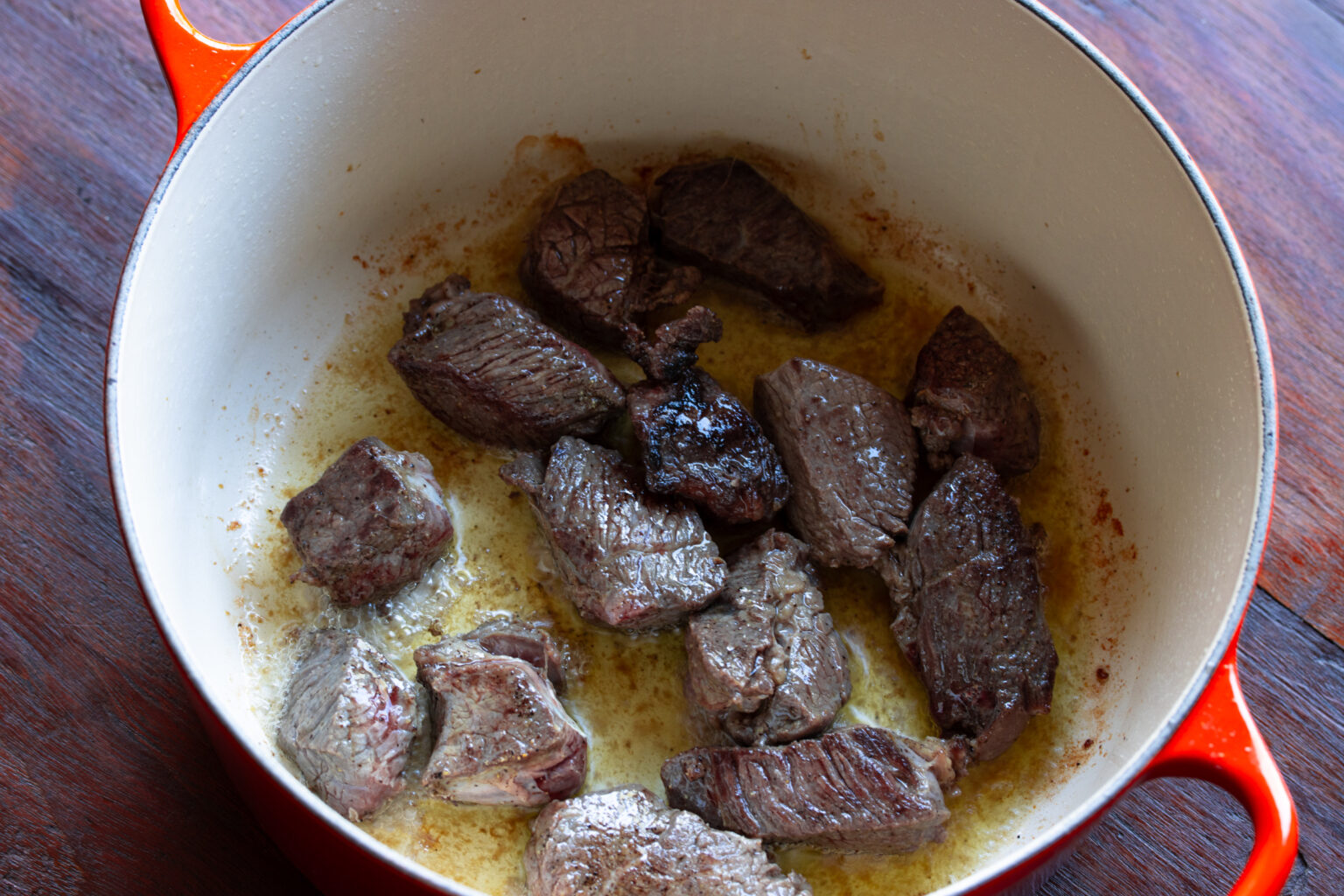 Pieces of meat being sauted in Dutch oven. 