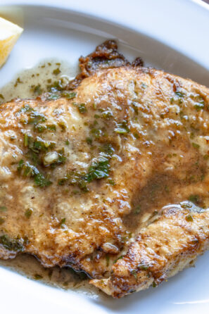 Chicken Francese served in a white oval dish with lemon wedges alongside and sauce poured over it.