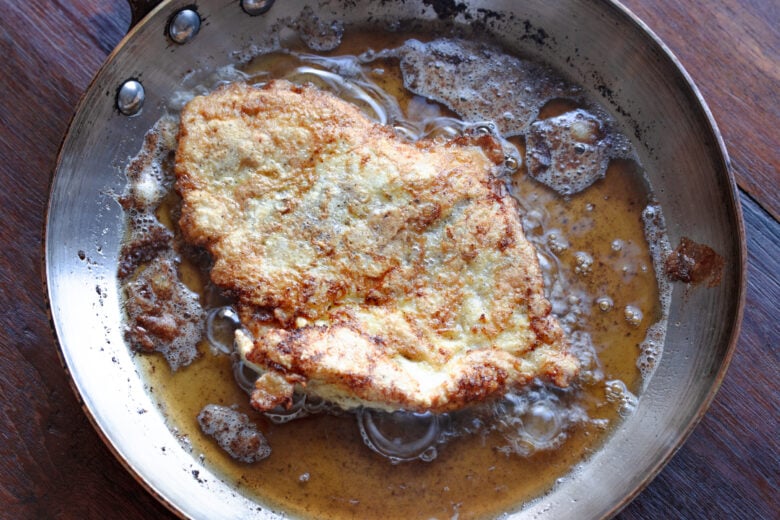 Chicken cutlets cooking in a large skillet, one at the time not to crowd the pan. 