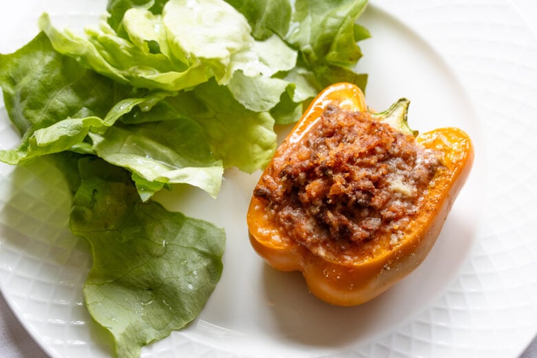 Half of a stuffed bell pepper on a white plate served with butter lettuce with vaingrette.