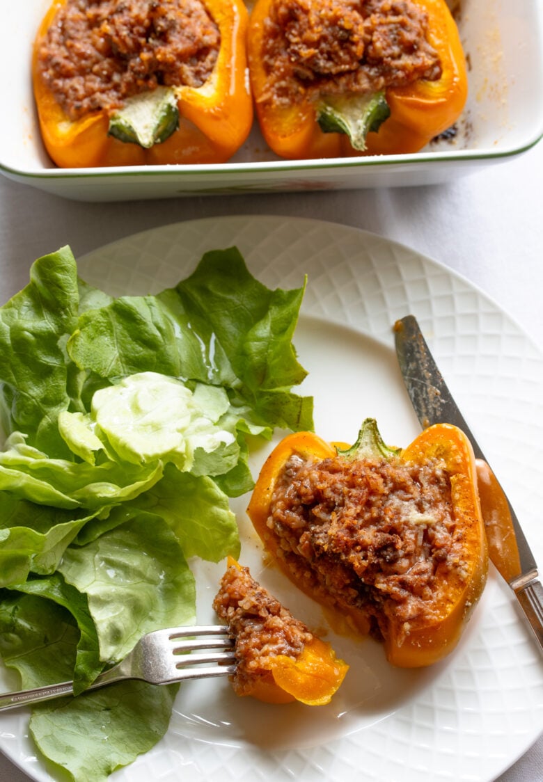 Stuffed bell peppers ready to be enjoyed on a white plate with green salad alongside.