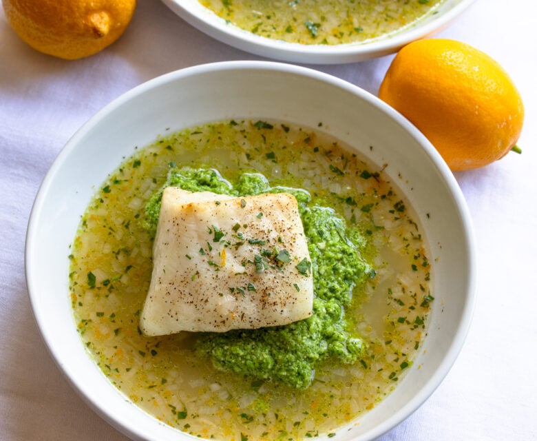 Sea bass placed over the pea puree surrounded by lemon soup in a white bowl.
