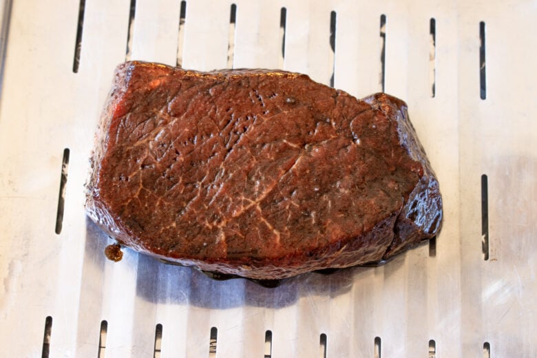 Marinated London broil steak placed on a broiler pan and ready to go in the oven.