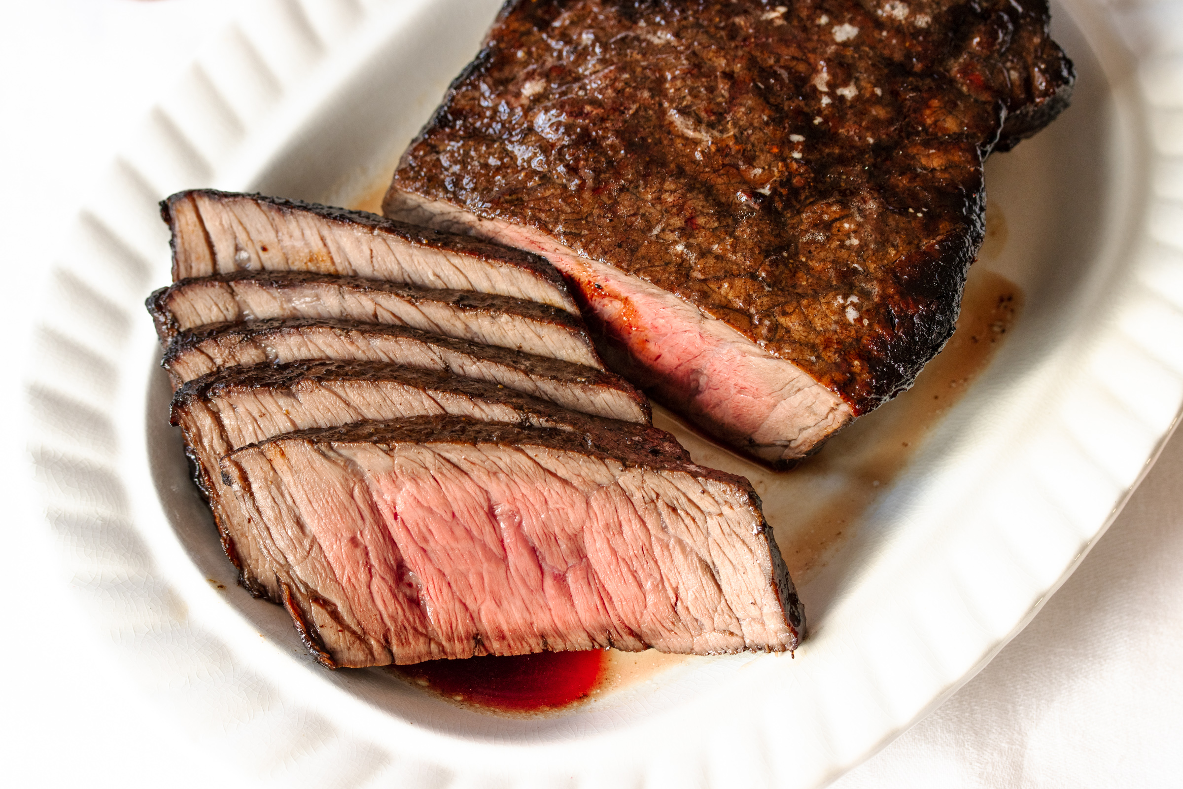 Sliced London broil served in an oval serving dish with balsamic glaze on the side.