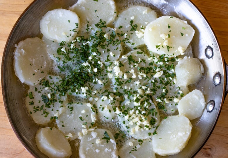 Potato rounds in a skillet over melted butter with garlic and chopped parsley.