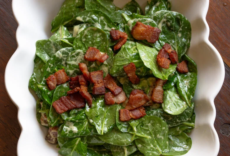 Spinach salad with warm bacon dressing served in a white scalloped serving bowl. 