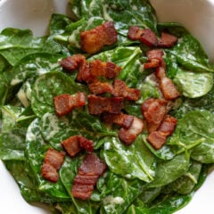 Spinach salad with warm bacon dressing served in a white scalloped serving platter.