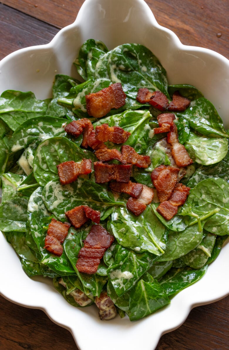 Spinach salad with warm bacon dressing served in a white scalloped serving platter.