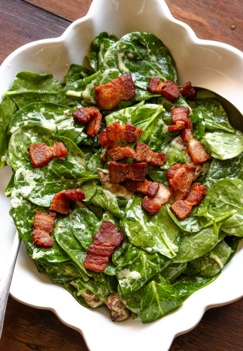 Spinach salad with warm bacon dressing in a white square serving dish.