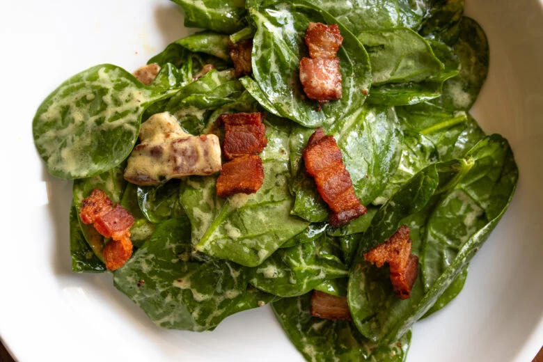 Spinach salad with warm bacon in a white salad plate. 