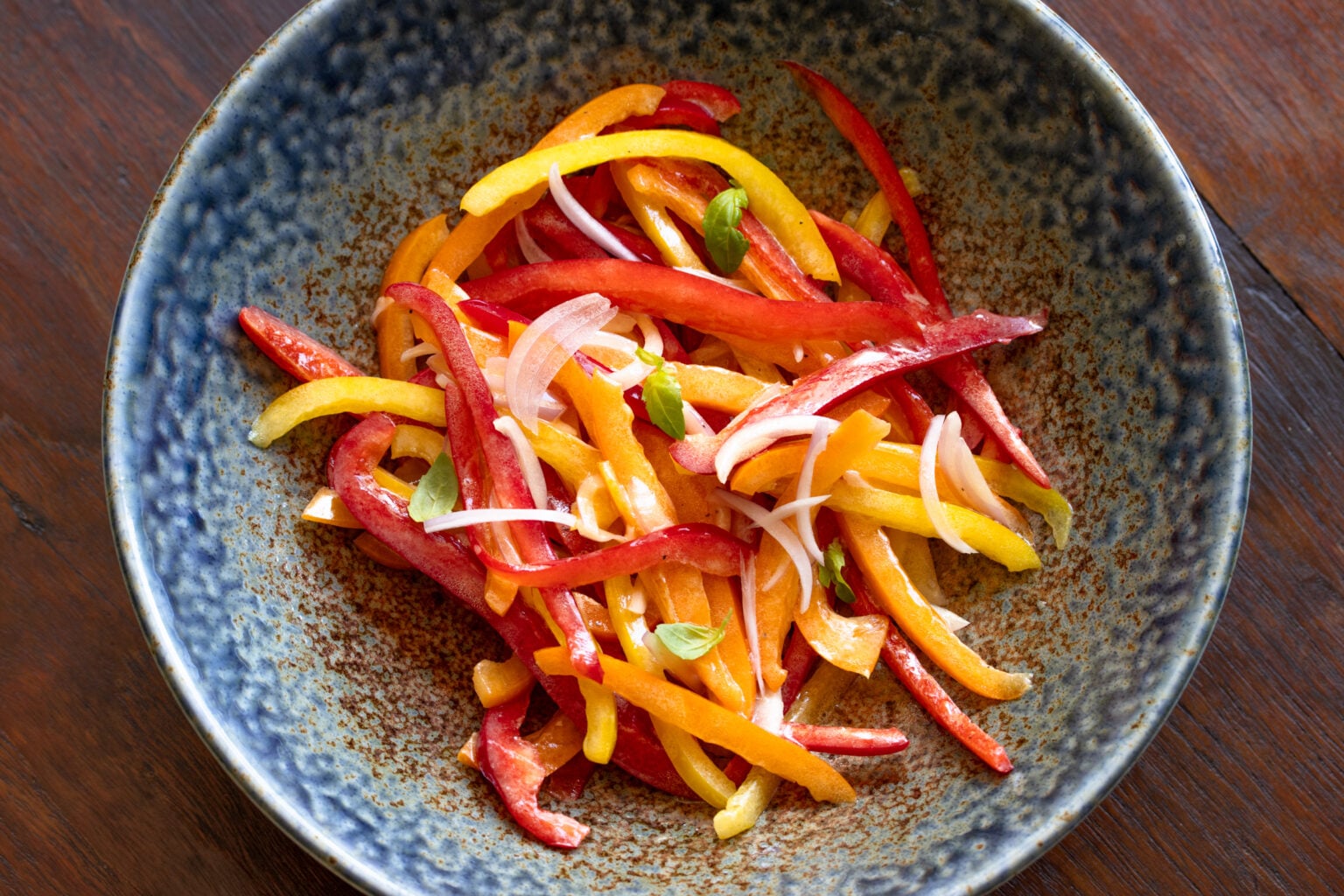 Bell pepper salad placed into a brown blue serving dish. 