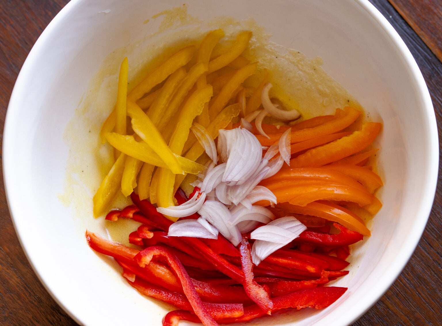 Bell peppers and shallots placed into the bowl with the vinaigrette. 