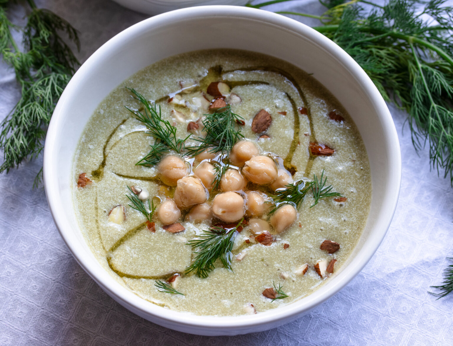Finished soup served in white soup bowls surrounded by dill and mint. 