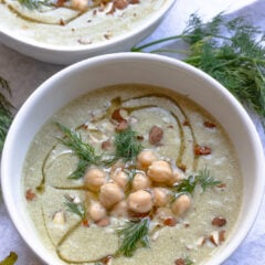 Cold cucumber soup with garbanzo beans served in white bowls topped with chopped almonds.