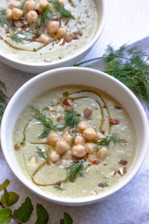 Cold cucumber soup with garbanzo beans served in white bowls topped with chopped almonds.