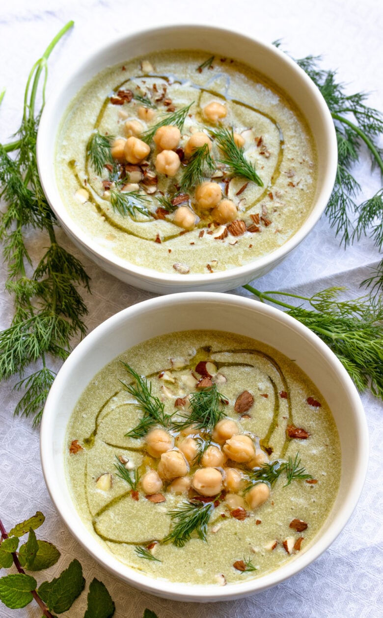 Cold cucumber soup with garbanzo beans served in white bowls topped with chopped almonds.