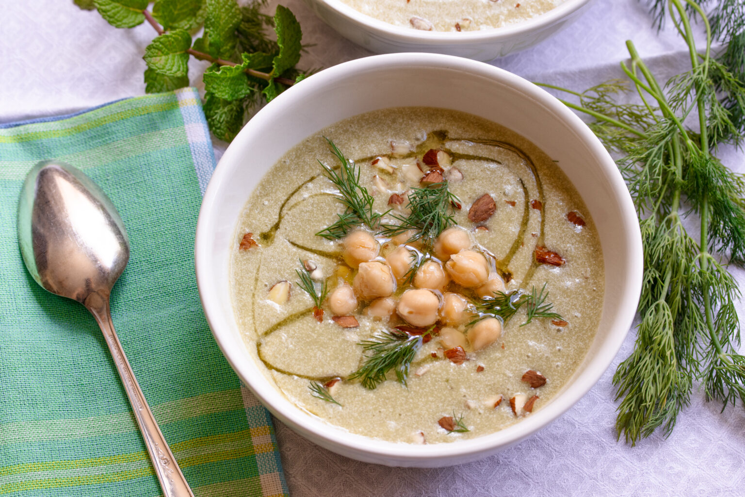 Cucumber soup recipe served in a white bowl with a serving spoon alongside. 