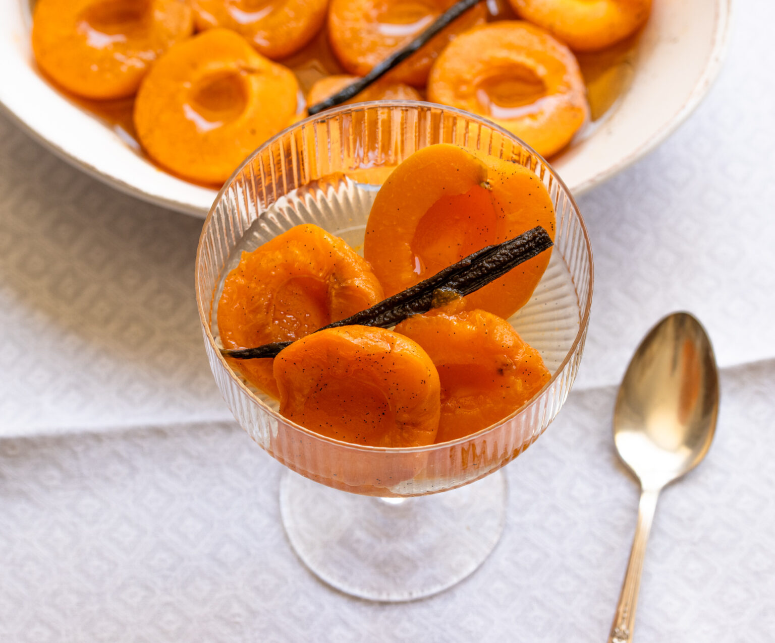 Apricots served in a tall wide mouth glassware with a spoon alongside.