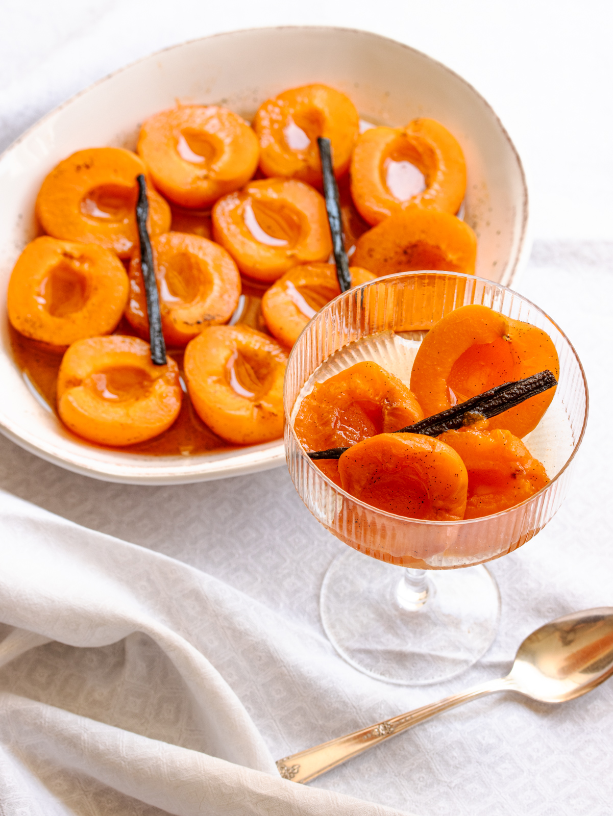 Apricot dessert served in a oval white plate and a few apricots served in a champagne coupe.