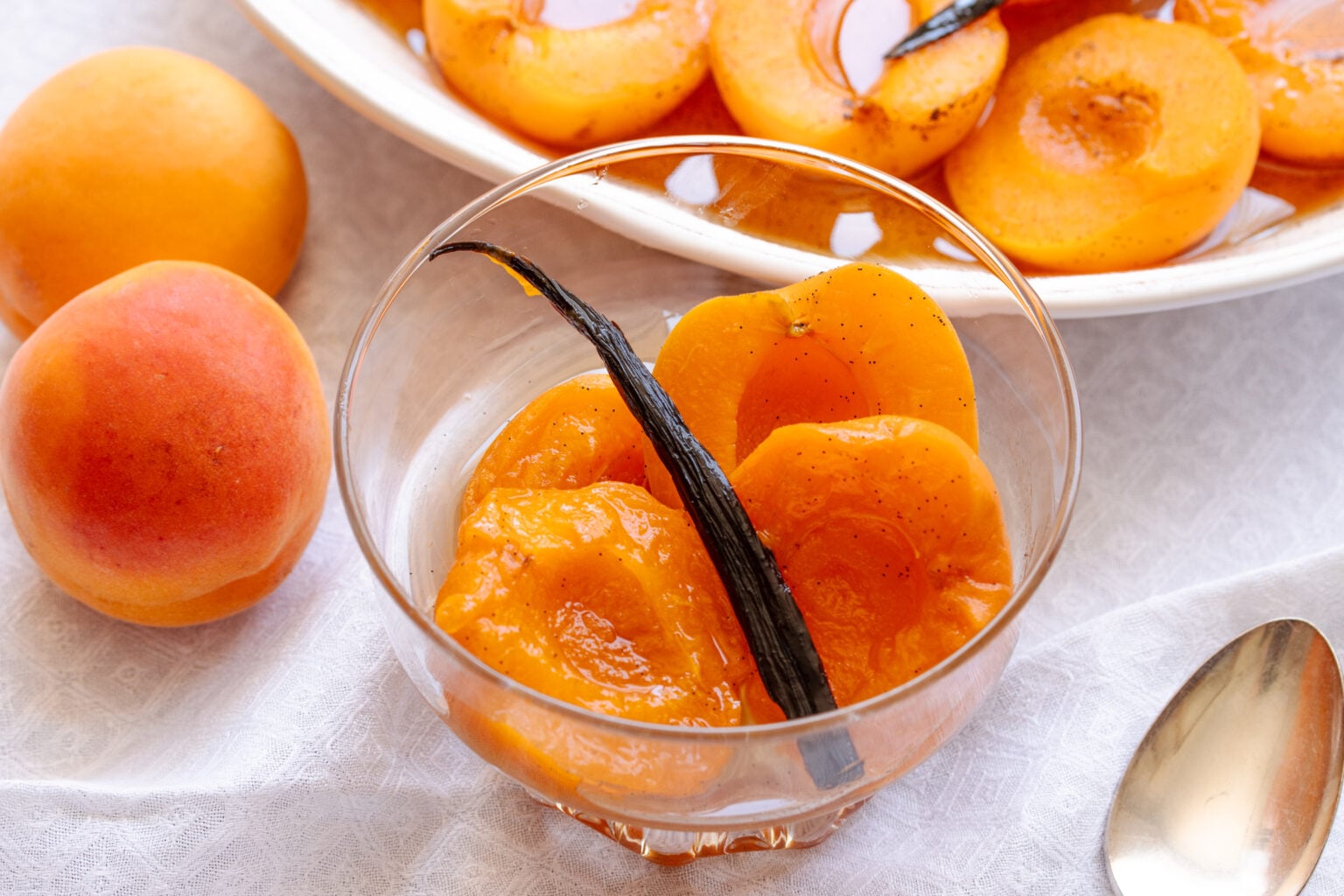 Poached apricots served with the vanilla bean in a glass dessert coupe with a spoon.