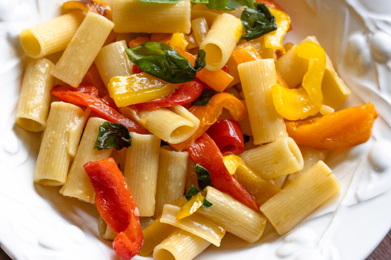 Close up of the roasted bell pepper sauce with the pasta in a white large rimmed pasta dish.