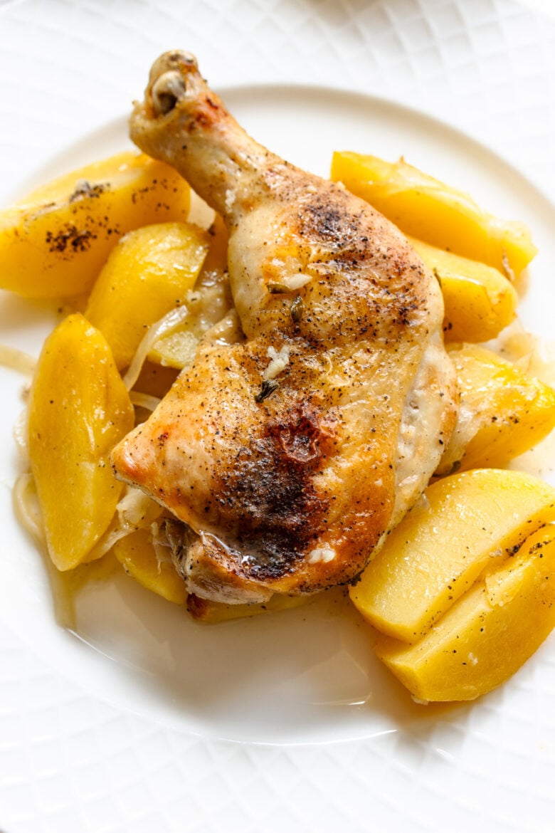 Greek lemon chicken and potatoes served on a cream white plate.