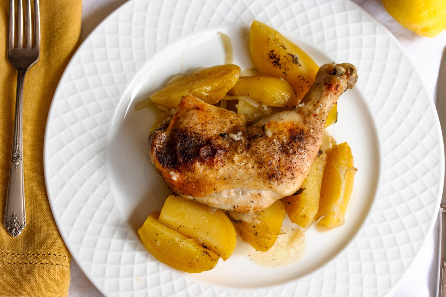 Greek lemon chicken served on a white plate alongside a mustard color napkin and serveware.