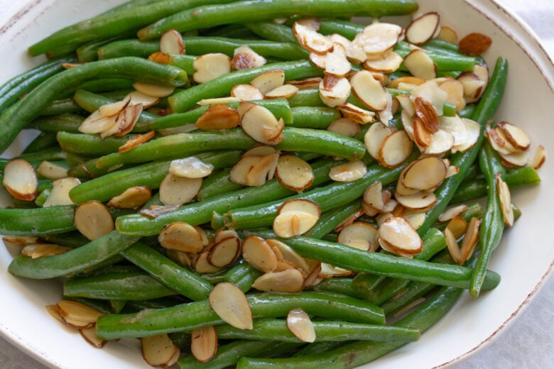 Green bean almondine served in an oval cream color serving plate.