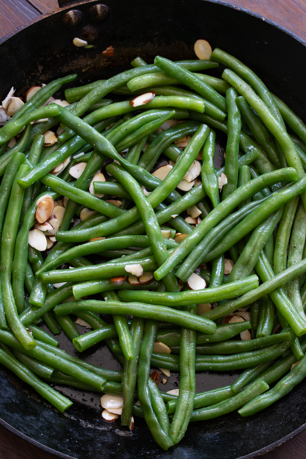 Green beans added to the almonds in the skillet to be sautéed.