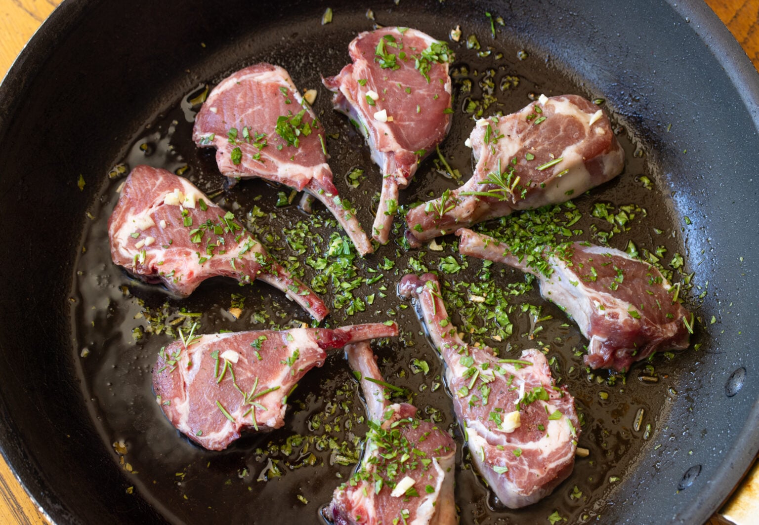 Lamb chops placed in a circular pattern in a large skillet. 
