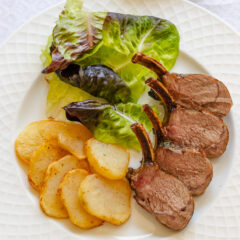 Roasted rack of lamb served alongside salad and potatoes on a white dish.