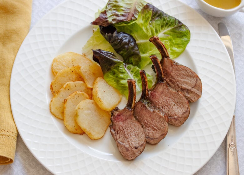 Roasted rack of lamb sliced and served on a plate with potatoes and salad. 