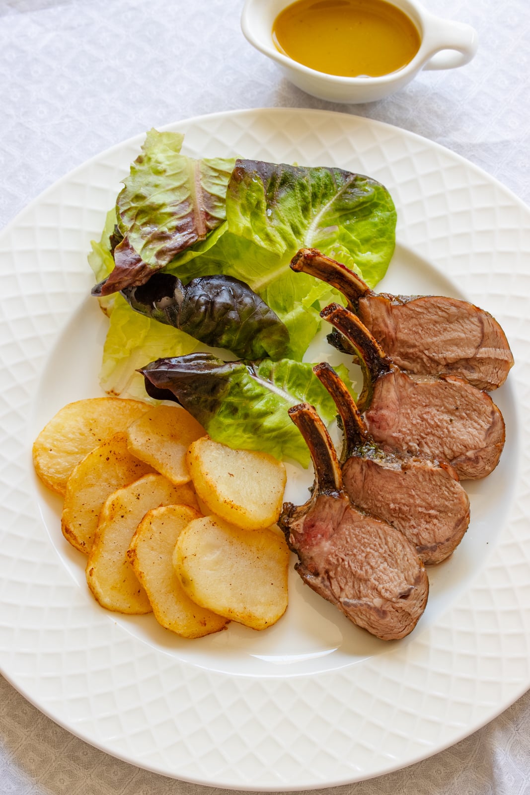 Roasted rack of lamb served alongside salad and potatoes on a white dish.
