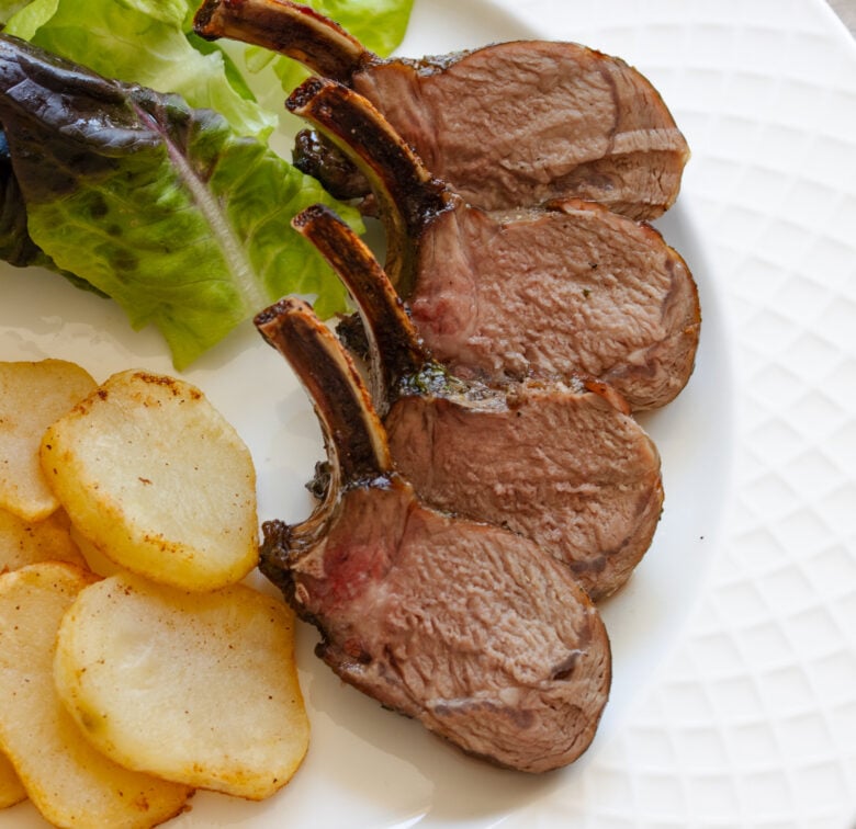 Roasted rack of lamb with caramelized crust served on. a white plate.