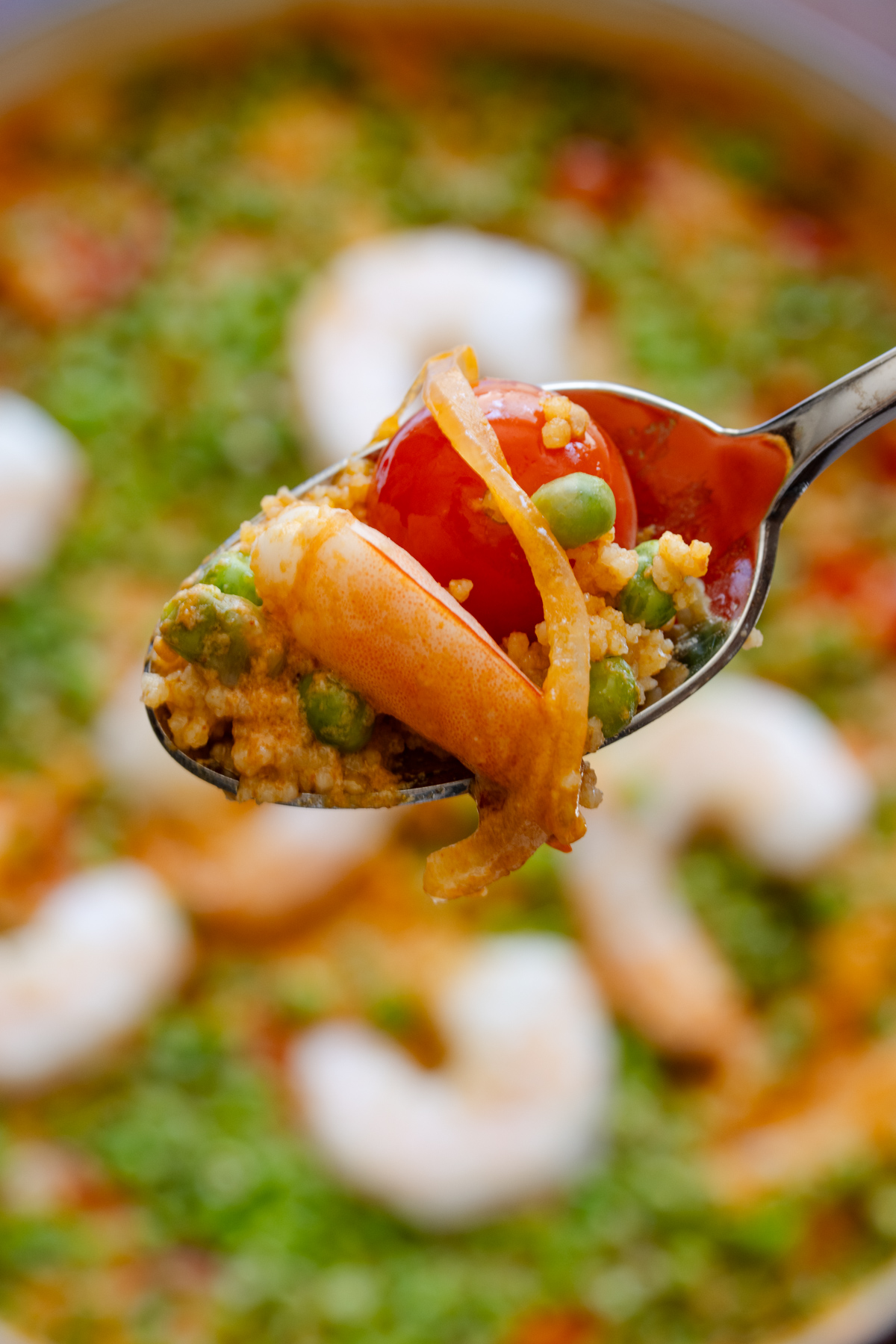 Spoonful consistent of a shrimp, half tomato and peas.