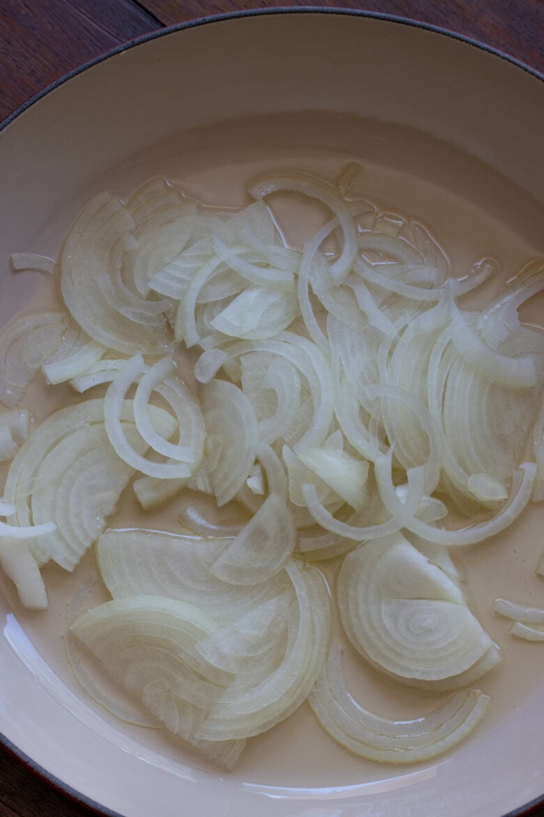 Sliced onions sautéing with olive oil in a round large skillet.