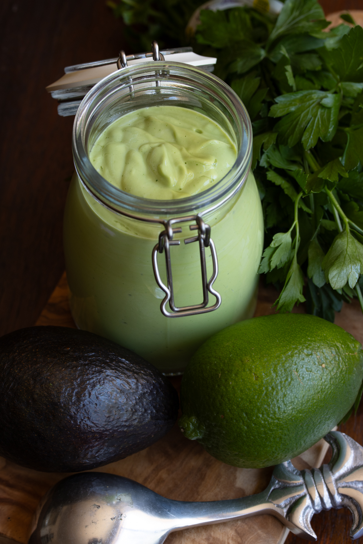 Avocado dressing served in a jar surrounded by lime, parsley and avocado.