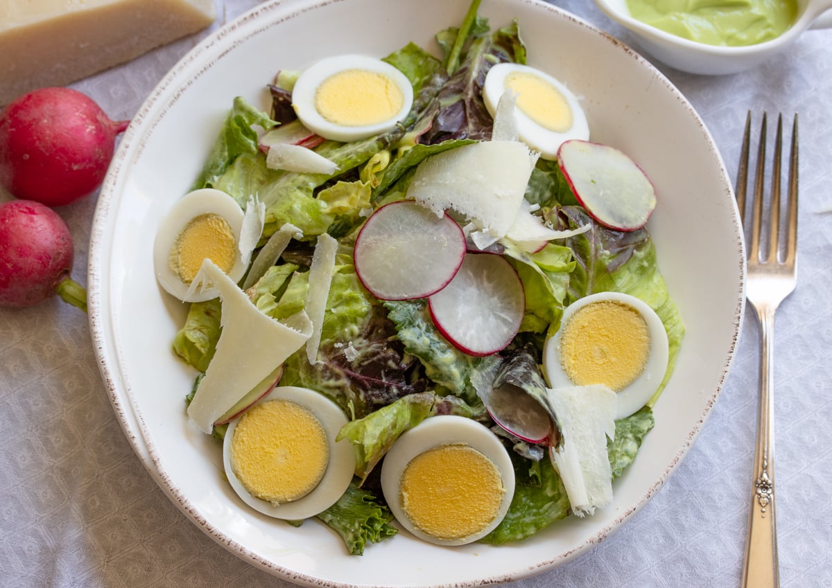 Avocado dressing in a mixed green salad served in a white salad dish.
