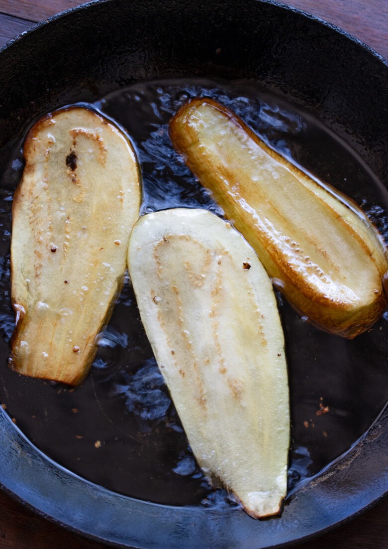 Slices of eggplant frying in a skillet.