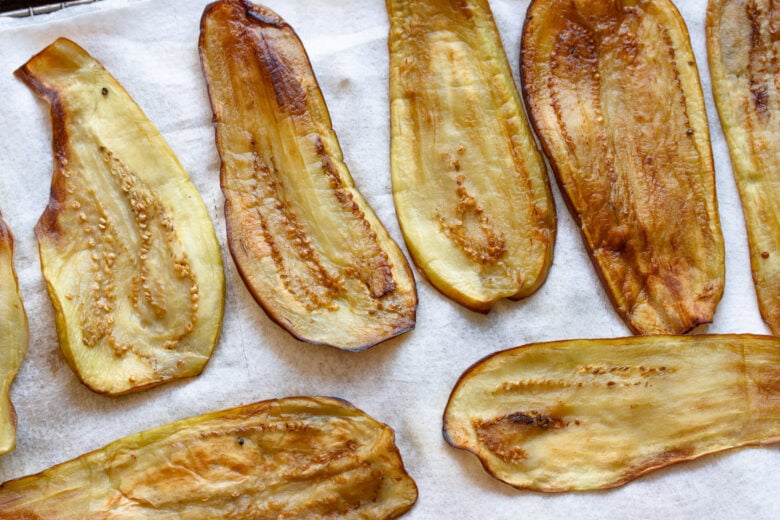 Cooked eggplant resting on paper towel over cooling rack.