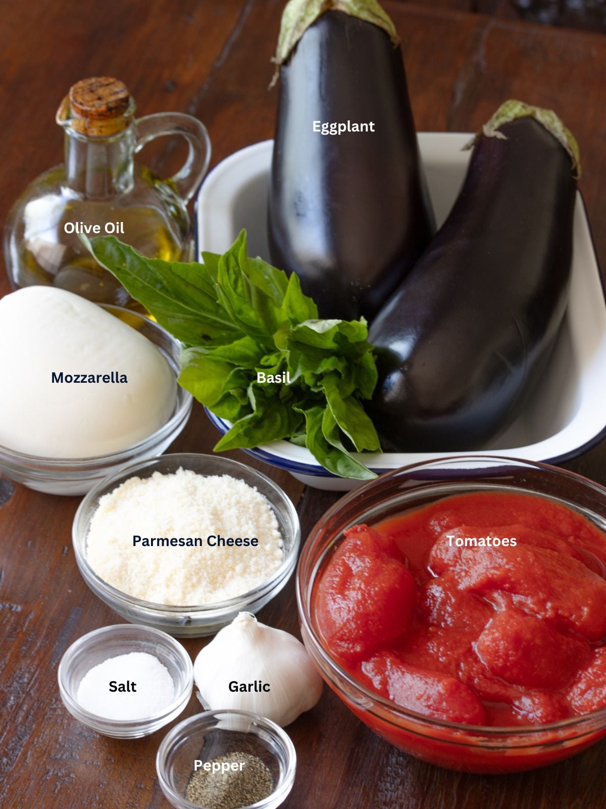 Eggplant parmigiana ingredients including eggplant, San Marzano tomatoes, mozzarella, Parmesan, garlic, and basil.