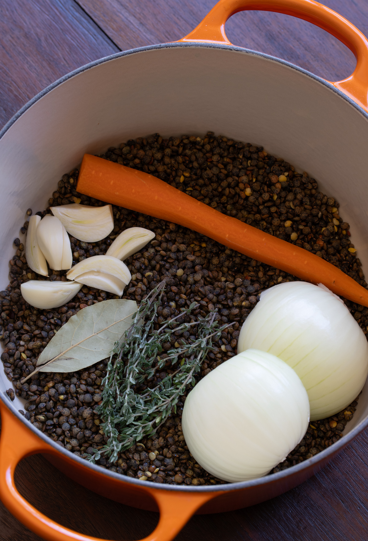 Green lentils, carrot, onion and herbs are ready to be cooked in a saucepan.
